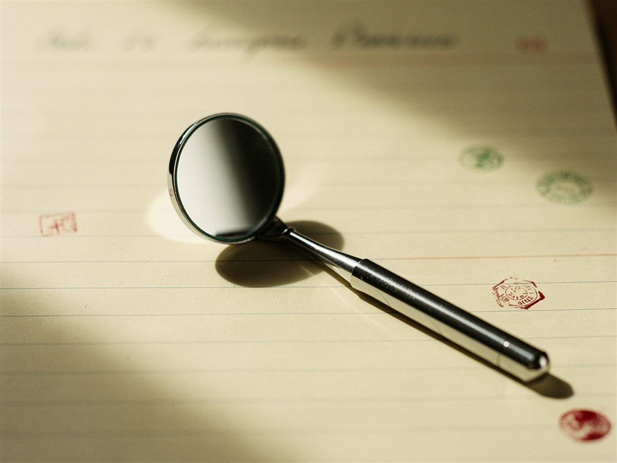 Dental mirror instrument resting on cream ledger paper with red and green ink marks